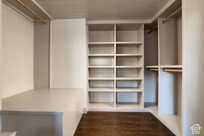 Custom walk-in closet featuring extensive built-in shelving, integrated wood hanging rods, wood-finish flooring, and a low-profile storage platform