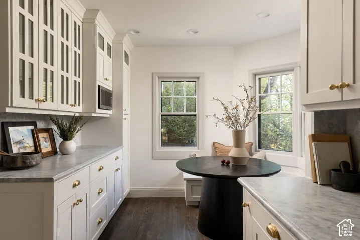 Custom cabinetry with glass-paneled upper doors, stone-surface countertops, recessed lighting, double-hung windows, and wood-finish flooring