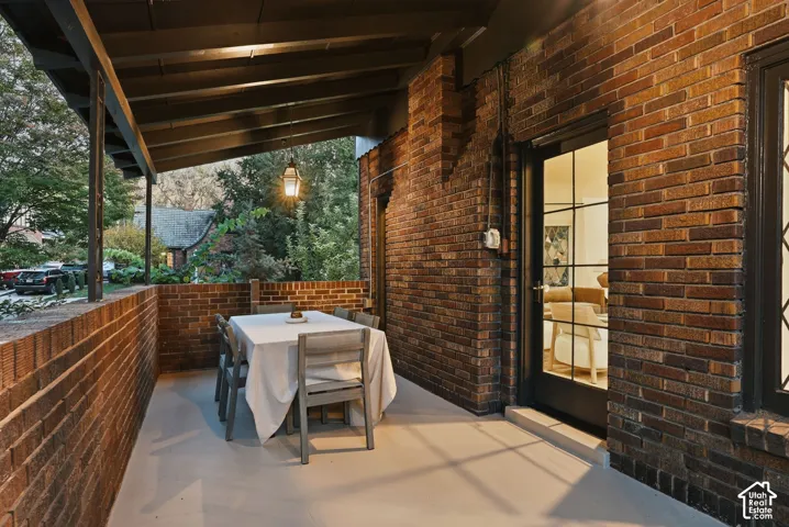 Covered patio featuring exposed brick walls, dark-toned beam ceiling, and a multi-pane glass door with dark trim