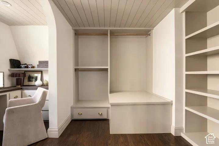 Custom built-in cabinetry featuring integrated shelving, hanging rods, and storage drawers under a plank-style ceiling with an arched entryway