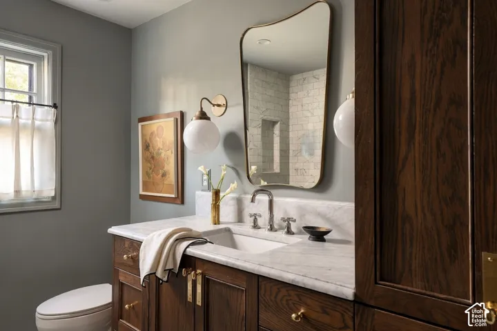 Custom dark wood vanity with stone countertop and integrated sink, accompanied by a contoured wall-mounted mirror, globe-style brass lighting, and high-contrast tile shower enclosure