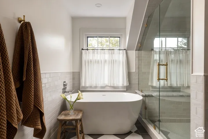 Freestanding soaking tub, walk-in glass-enclosed shower with brass hardware, subway tile wall surround, and geometric patterned floor tile
