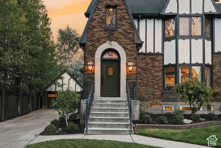 Tudor-style exterior featuring brick facade with timber-frame detailing, arched entryway, diamond-pane leaded glass windows, concrete staircase with iron railings, and detached garage