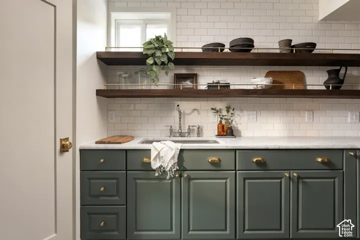 Shaker-style cabinetry in a sage finish, stone countertop with an undermount sink, white subway tile backsplash, and dual floating wood shelves with brass gallery rails