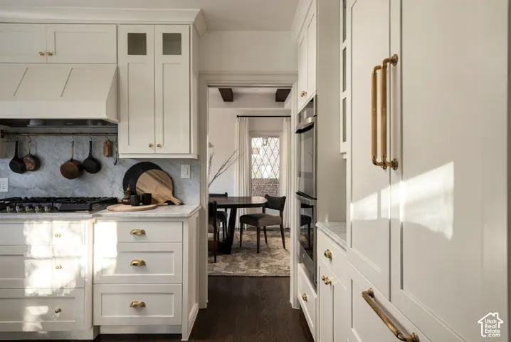 Kitchen featuring light-toned cabinetry with brass hardware, stone slab backsplash, integrated double wall ovens, and wood-finish flooring