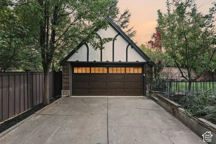 Detached garage featuring Tudor-style architectural detailing, a wood-finish sectional door with transom windows, brick and stucco exterior, and a private concrete driveway