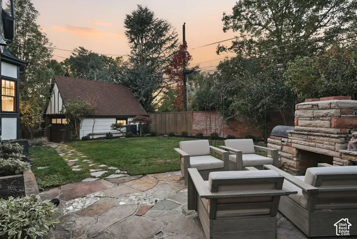 Backyard featuring a natural stone patio, custom masonry outdoor fireplace, detached garage, and mature landscaping