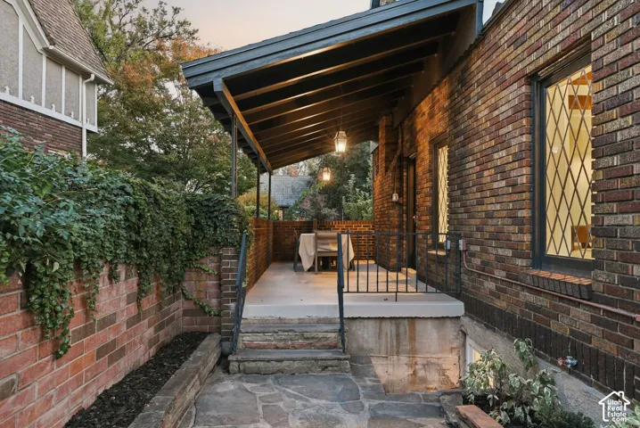 Covered outdoor terrace featuring a brick exterior, stone patio, iron railings, and diamond-pane windows