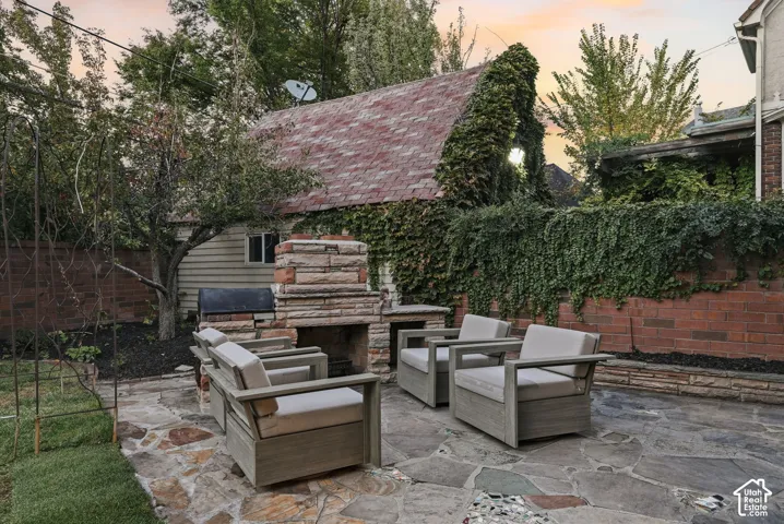 Outdoor stone patio featuring a stacked-stone fireplace, low-profile brick perimeter wall, and established climbing ivy