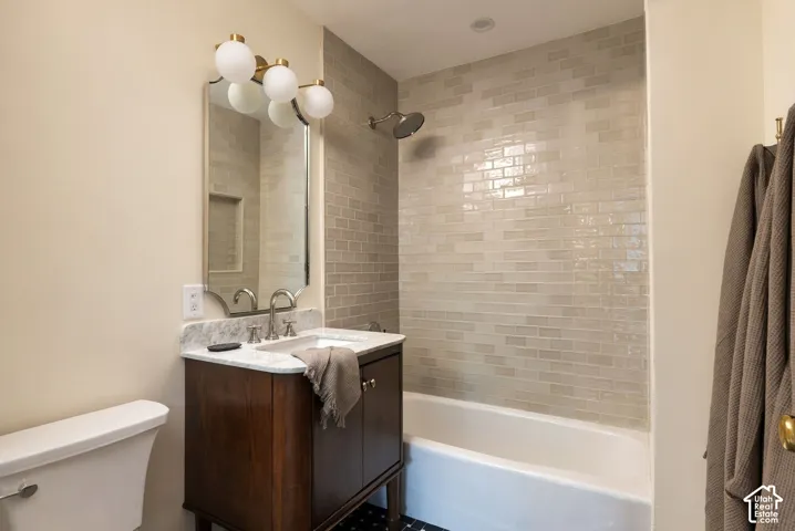 Bathroom featuring a dark wood-finish vanity, stone-pattern countertop with an integrated sink, polished metal wall-mounted three-globe light fixture, scalloped-edge mirror, and horizontal tile shower surround