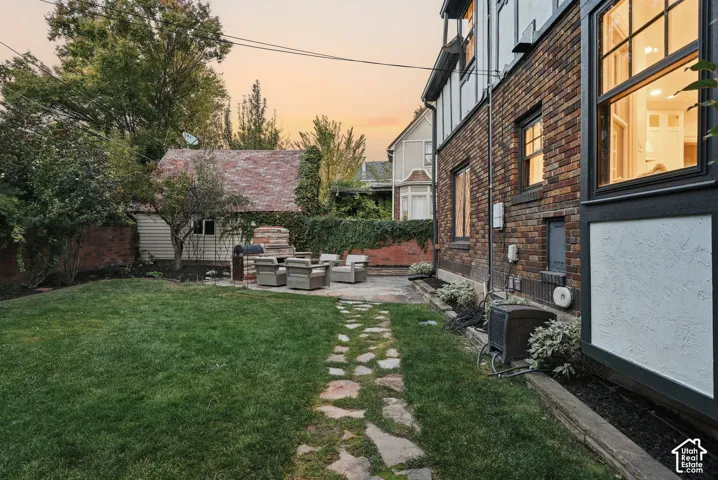 Exterior backyard featuring brick masonry wall, stone paver pathway, built-in outdoor stone fireplace, and manicured lawn