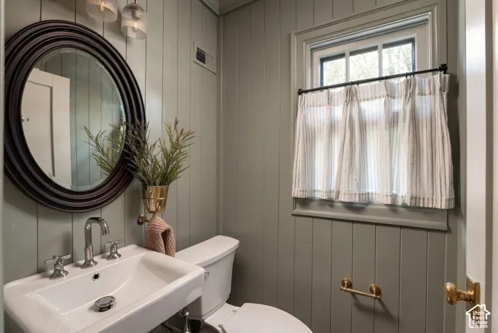 Vertical wood-paneled walls, pedestal sink with polished chrome widespread faucet, circular framed mirror, and brass hardware fixtures