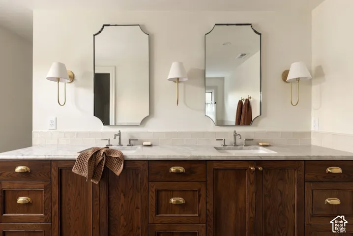 Dual-sink vanity featuring custom dark-stained cabinetry, stone-finish countertops, brass-tone hardware, arched-top wall mirrors, and wall-mounted sconce lighting