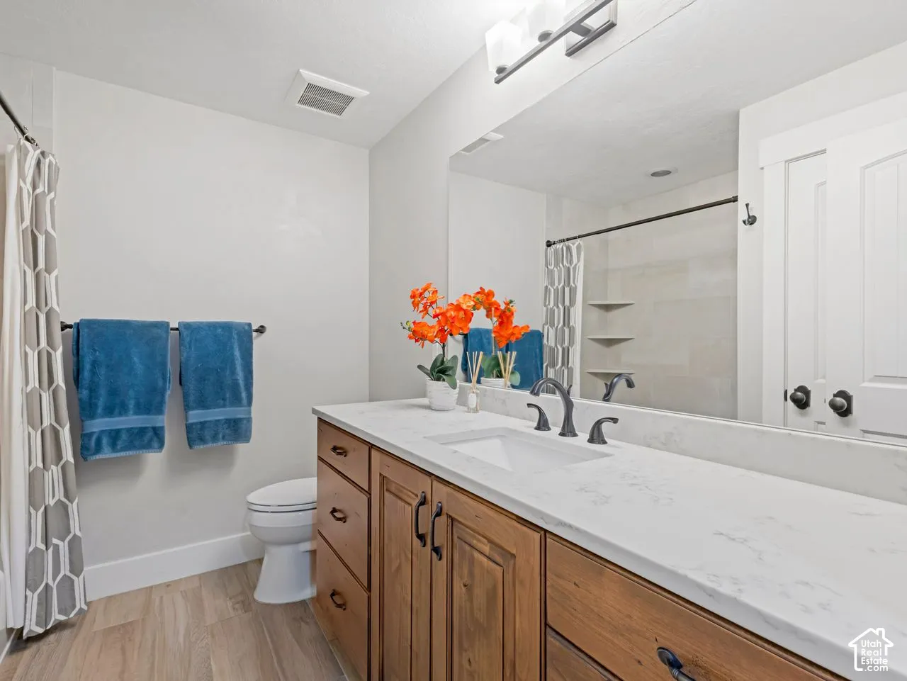 Bathroom featuring custom wood cabinetry, stone-finish countertops, an undermount sink with a widespread faucet, large wall-to-wall mirror, and wood-finish flooring
