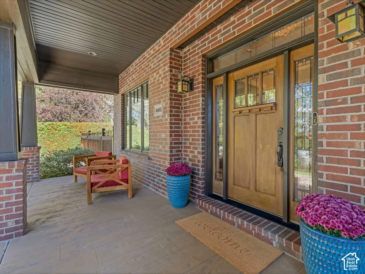 Covered front porch featuring a brick facade, wood-finish flooring, and a stained wood entry door with side light glass panels