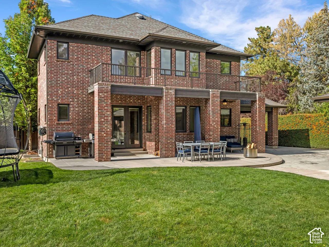 Two-story brick exterior featuring a concrete patio, second-level balcony with metal railing, and a fenced lawn
