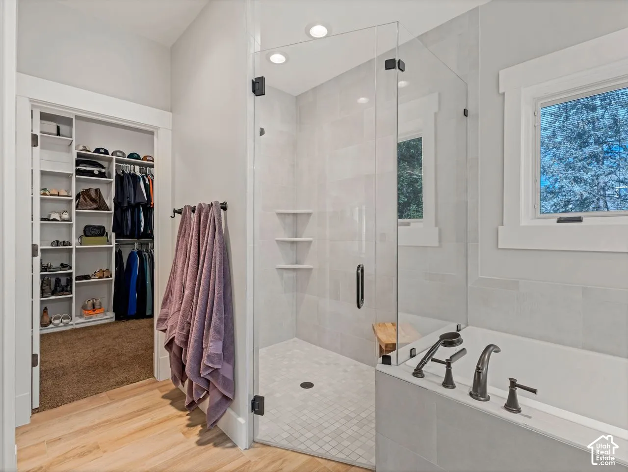 Walk-in closet with built-in shelving, glass-enclosed shower featuring stone-finish wall tile and recessed shelving, and a soaking tub with dark-finish hardware