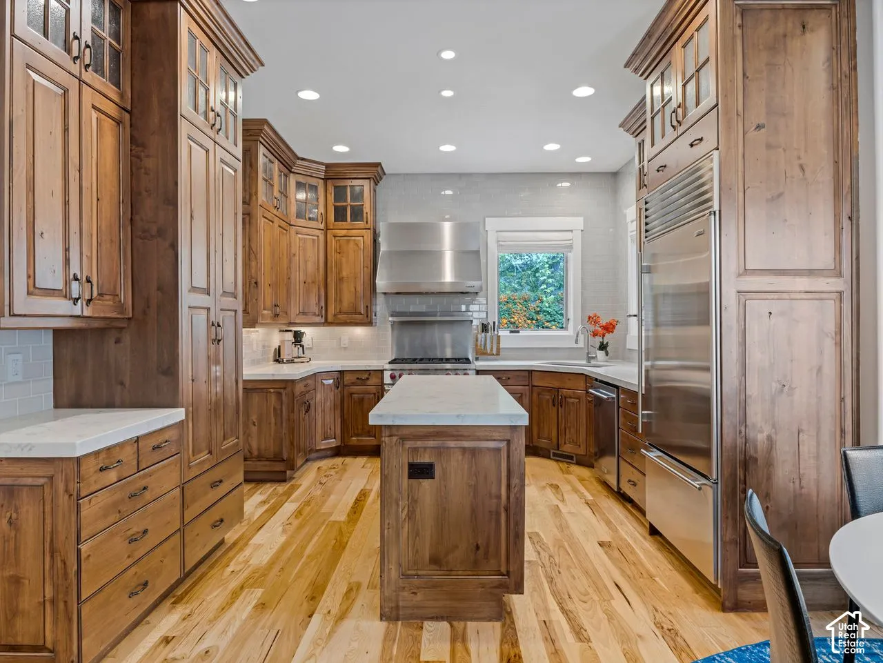 Kitchen featuring custom wood cabinetry, a central island with a stone countertop, stainless steel appliances, recessed ceiling lighting, and wood-finish flooring