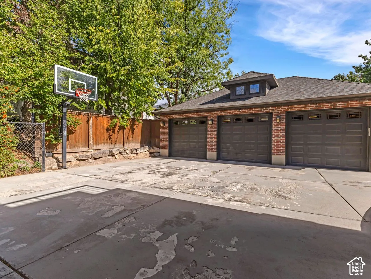 Three-car brick garage featuring a pitched roofline, recessed lighting, and a concrete driveway with an integrated basketball standard