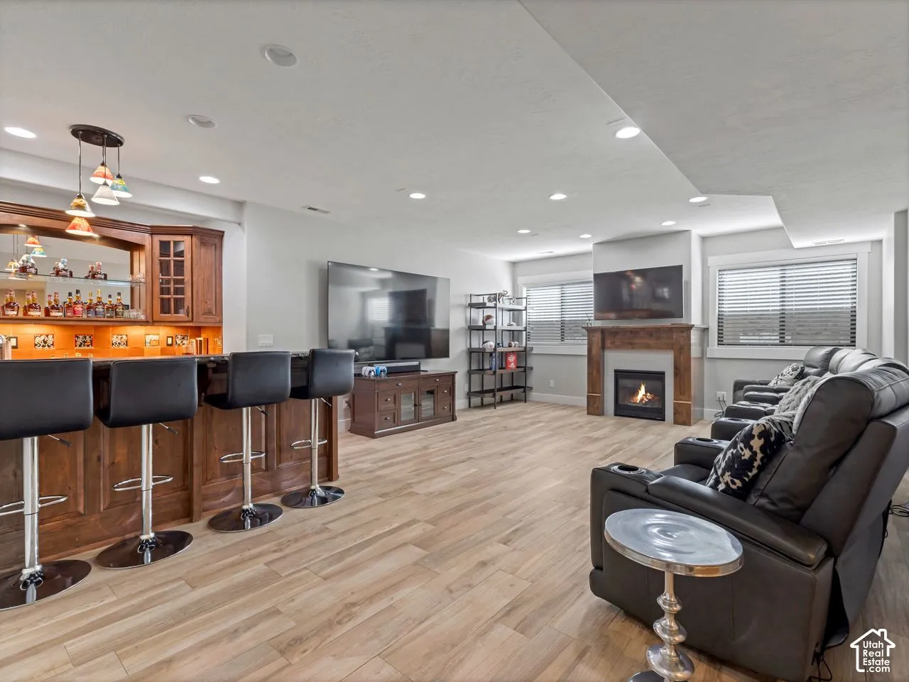 Built-in wood-finished wet bar with mirror backing and recessed lighting, gas fireplace with wood mantel, wood-finish flooring, and recessed ceiling lighting
