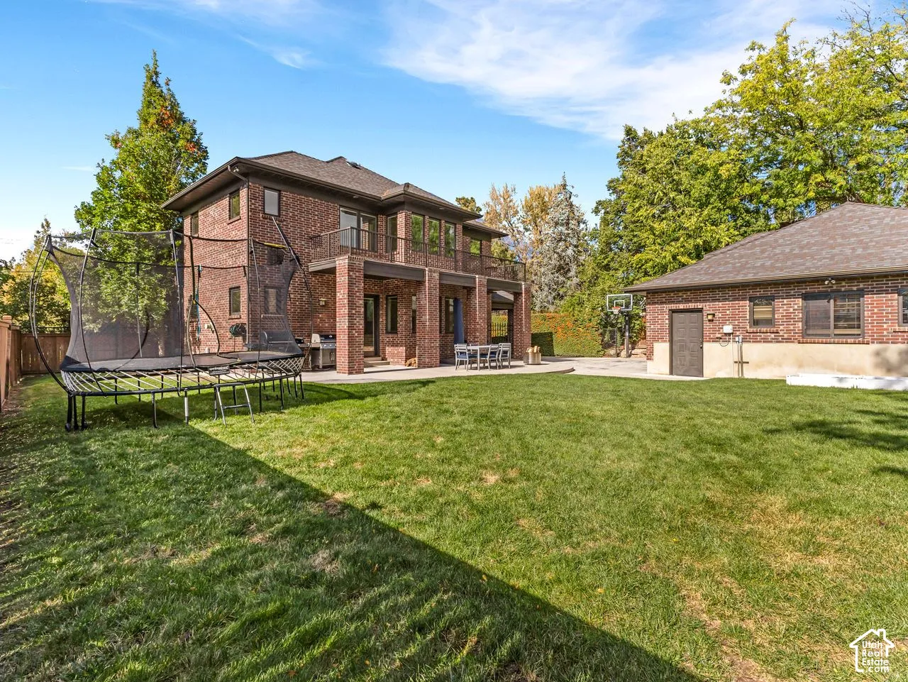 Multi-story brick exterior featuring a covered patio, second-story balcony, expansive lawn, and detached garage