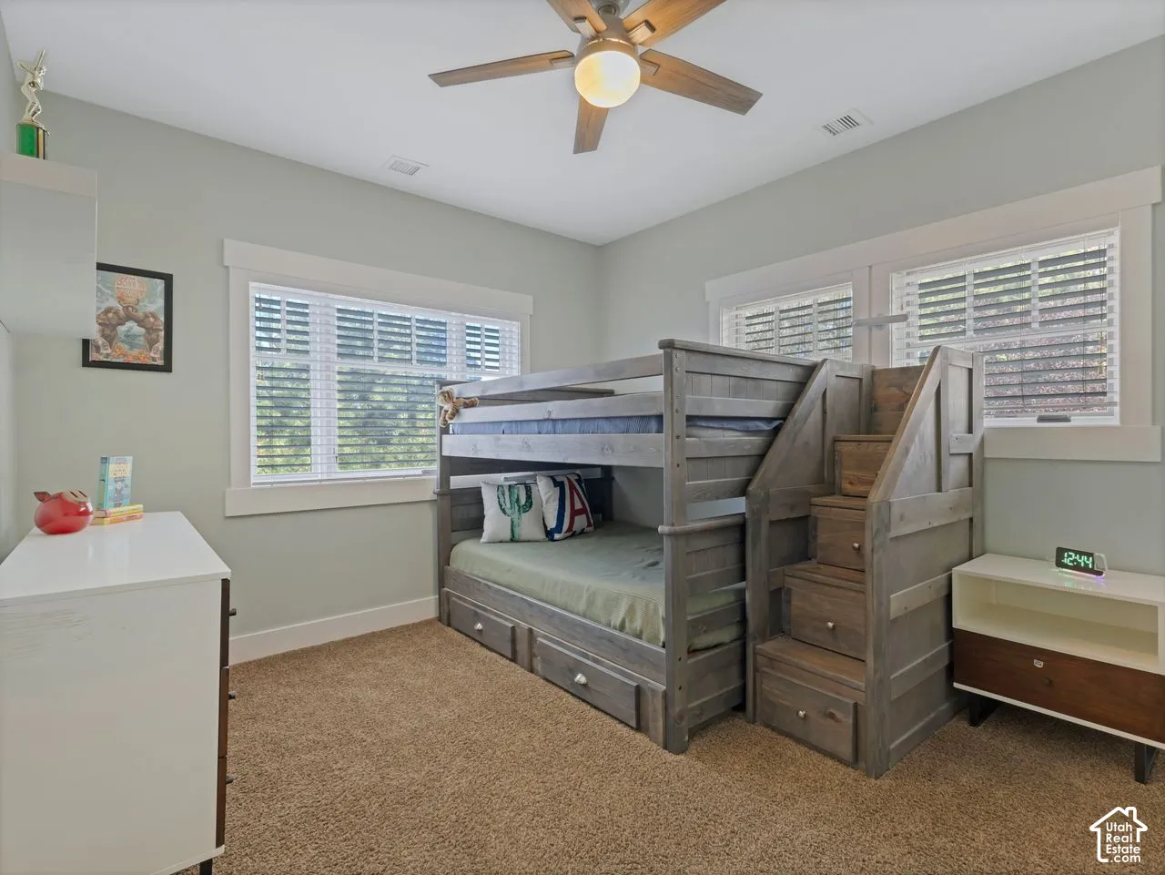 Bedroom interior featuring wall-to-wall carpeting, dual windows with white casings, and a central ceiling fan with integrated lighting