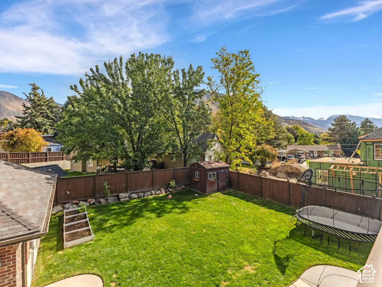 Expansive backyard featuring a level lawn, raised garden beds, storage shed, perimeter wood fencing, and mountain backdrop