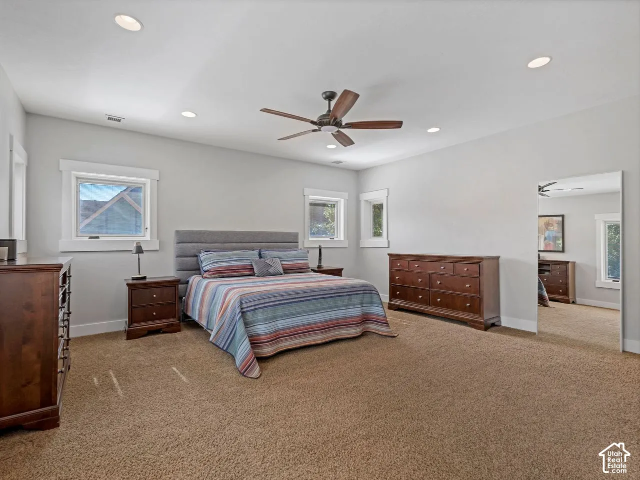 Spacious room featuring neutral wall tones, recessed lighting, carpeted flooring, a ceiling fan, and large windows with thick white trim