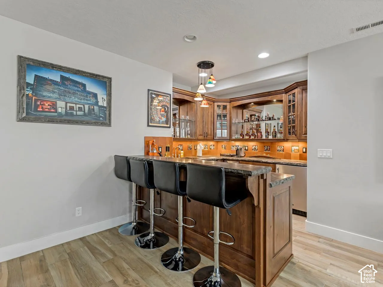 Built-in wood cabinetry with glass-front display sections, stone-finish bar top, under-cabinet lighting, integrated mirrored backsplash, and wood-finish flooring