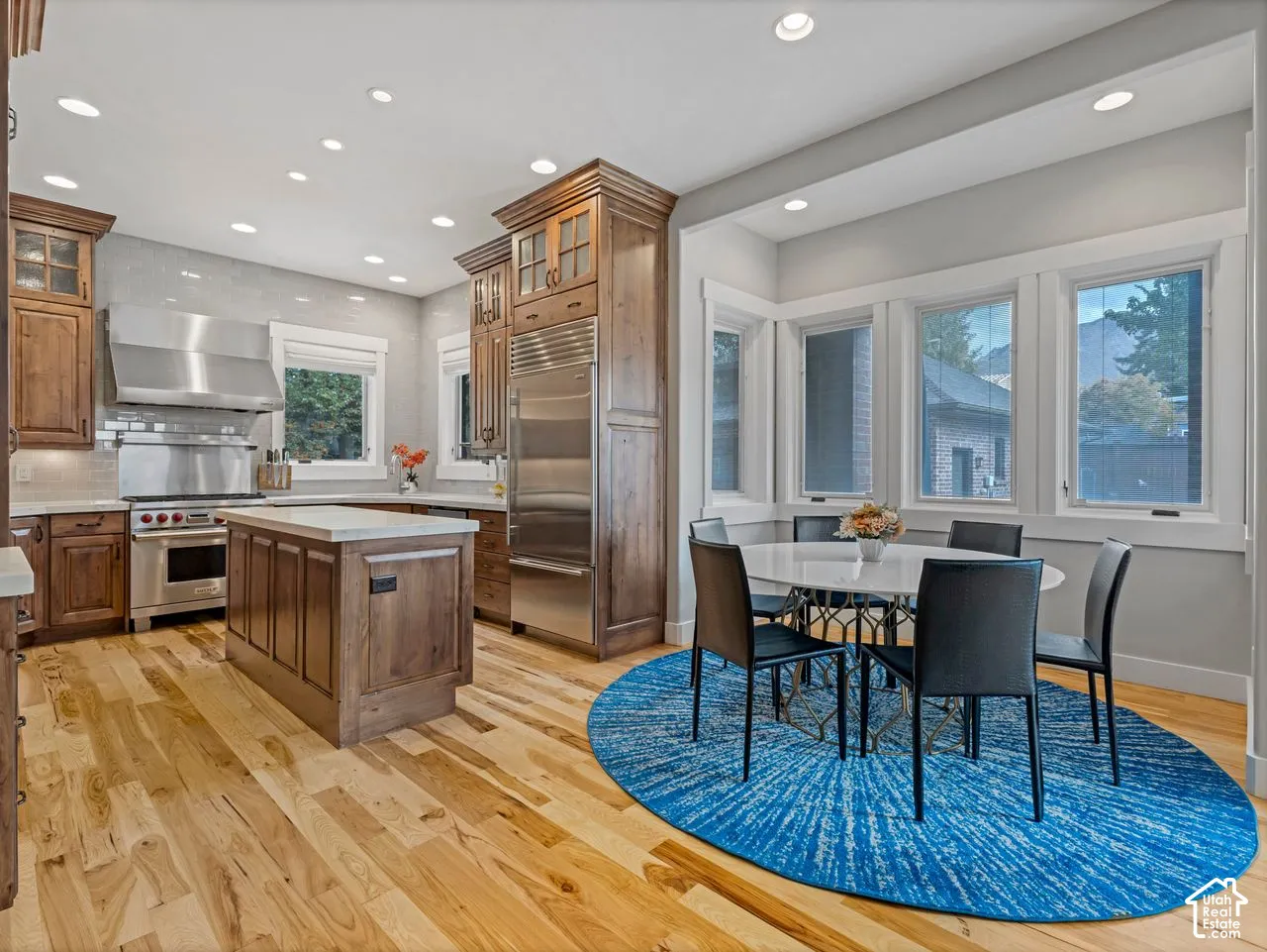 Kitchen featuring custom wood cabinetry, stainless steel professional-grade appliances, a central island with a stone countertop, recessed lighting, and wood-finish flooring