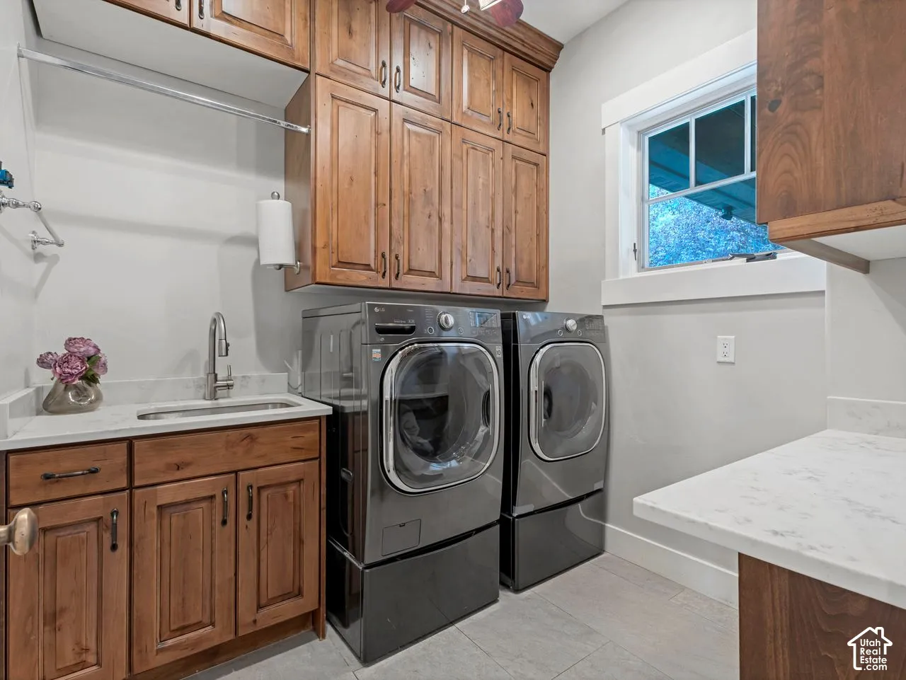 Laundry room featuring raised-panel wood cabinetry, stone-finish countertops, stainless steel undermount sink, and tile flooring