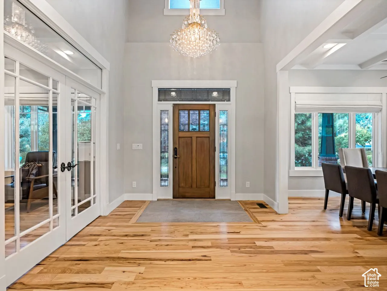 Entryway featuring high ceilings, wood-finish flooring, a crystal chandelier, and a wood-paneled door with decorative glass sidelights and transom