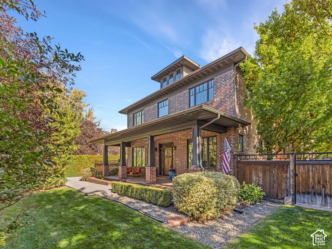 Multi-story brick exterior featuring a covered front porch with square columns, dormer window, and mature landscaping