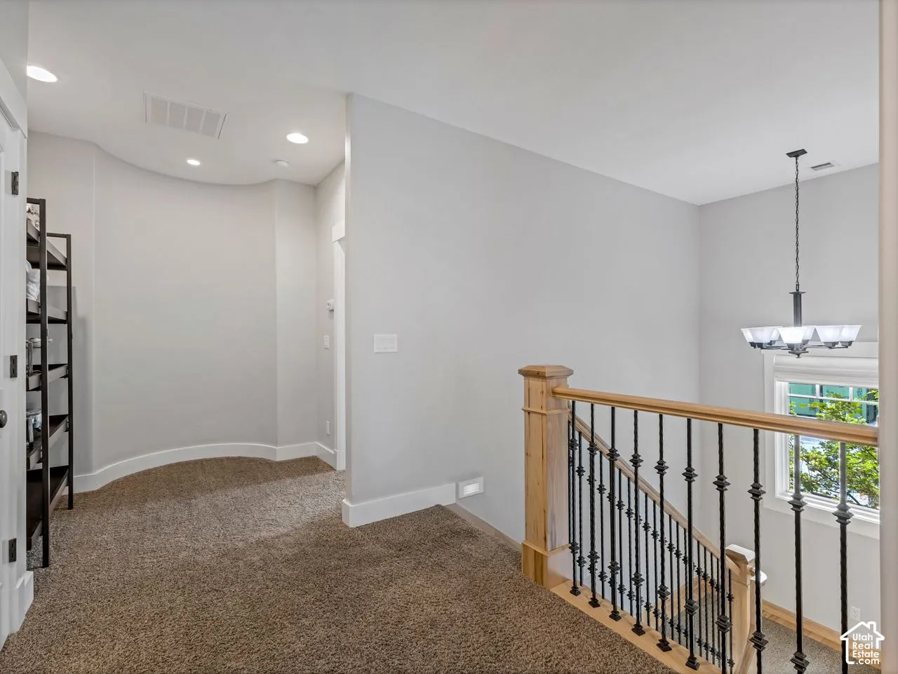 Curved wall detail featuring neutral wall tones, recessed lighting, and a staircase with natural wood handrails and black iron balusters, complemented by a multi-arm chandelier