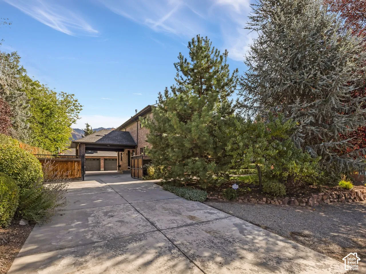 Multi-car garage with covered parking area, masonry exterior, and expansive concrete driveway featuring mature landscaping and stone retaining wall