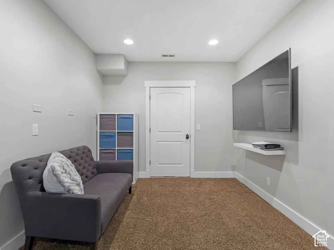 Interior room featuring neutral-toned carpeting, recessed ceiling lighting, a solid-core interior door with casing, and a wall-mounted floating shelf