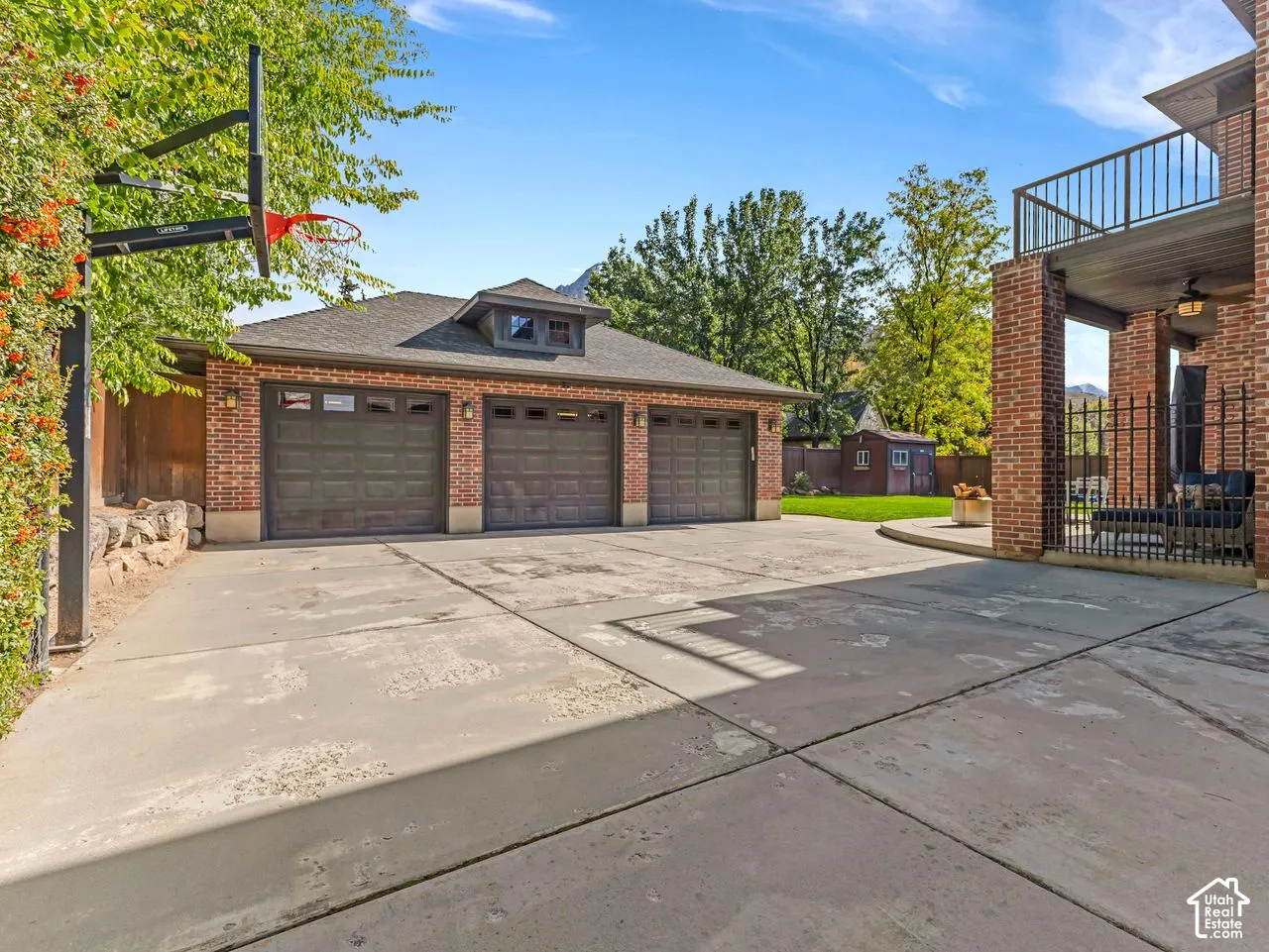 Three-car brick garage featuring a roof cupola and concrete driveway, complemented by a covered brick patio with a metal railing