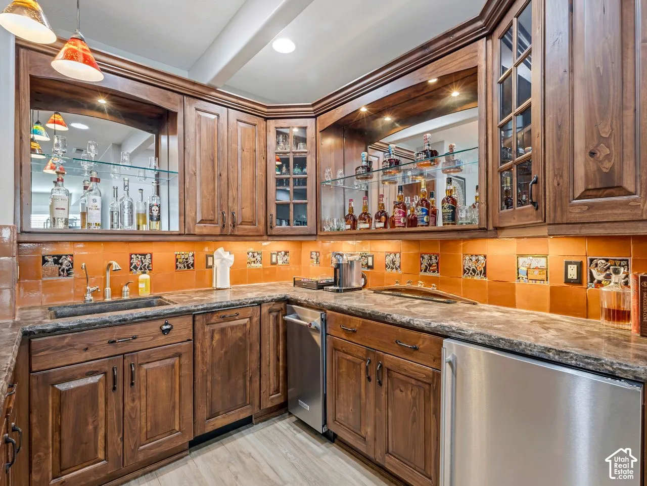Custom stained-wood cabinetry, stone-finish countertops, decorative ceramic tile backsplash, integrated glass shelving, and stainless steel under-mount sink
