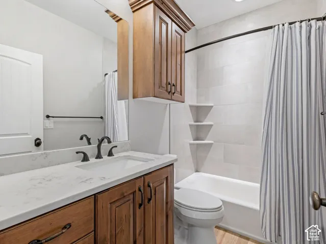 Wood-finish vanity with a stone-composite countertop, undermount sink, oil-rubbed bronze faucet, coordinating built-in cabinetry, and tile-surround tub with integrated corner shelving