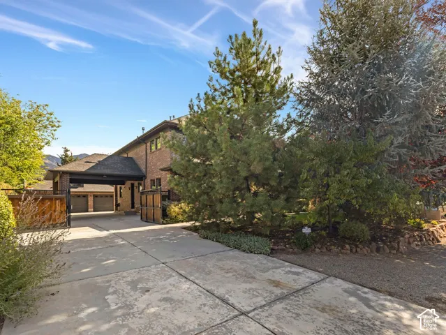 Brick exterior residence featuring a covered entryway, multi-car garage, concrete driveway, and mature landscaping