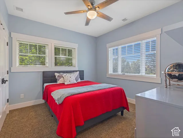Bedroom featuring carpeted flooring, multiple windows with thick casing, and a ceiling fan with integrated light fixture