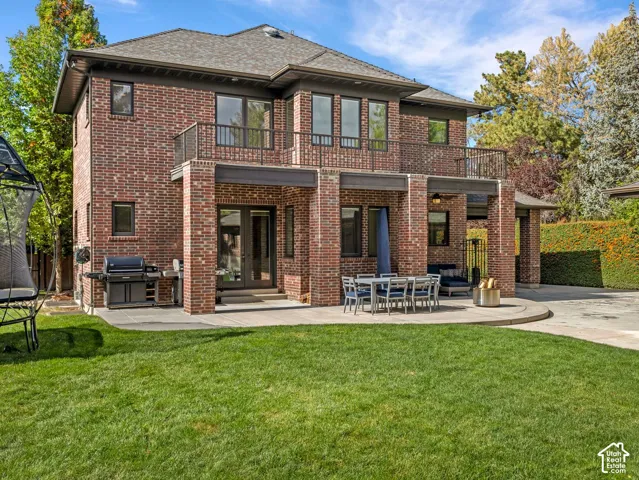 Two-story brick exterior featuring a concrete patio, second-level balcony with metal railing, and a fenced lawn