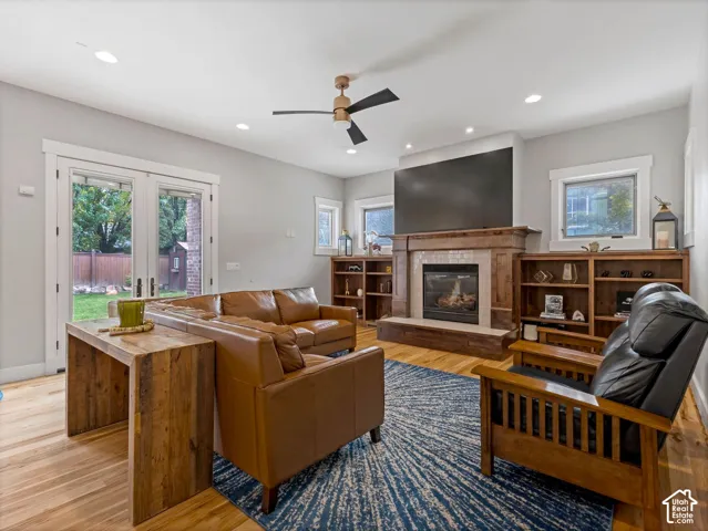 Fireplace with wood mantle and hearth, wood-finish flooring, built-in shelving, recessed lighting, and double glass doors