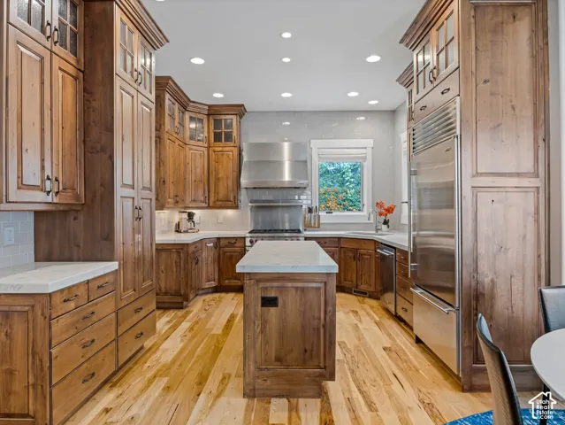 Kitchen featuring custom wood cabinetry, a central island with a stone countertop, stainless steel appliances, recessed ceiling lighting, and wood-finish flooring