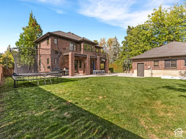 Multi-story brick exterior featuring a covered patio, second-story balcony, expansive lawn, and detached garage