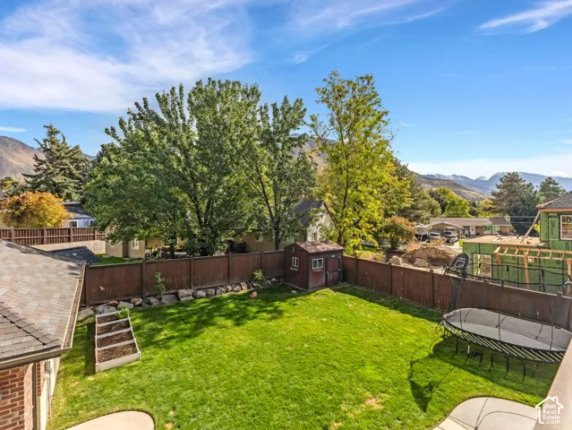 Expansive backyard featuring a level lawn, raised garden beds, storage shed, perimeter wood fencing, and mountain backdrop