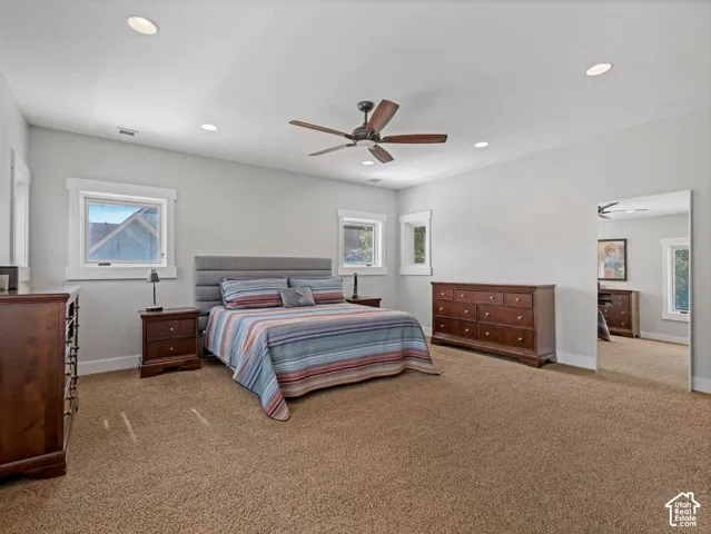 Spacious room featuring neutral wall tones, recessed lighting, carpeted flooring, a ceiling fan, and large windows with thick white trim