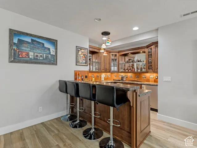 Built-in wood cabinetry with glass-front display sections, stone-finish bar top, under-cabinet lighting, integrated mirrored backsplash, and wood-finish flooring