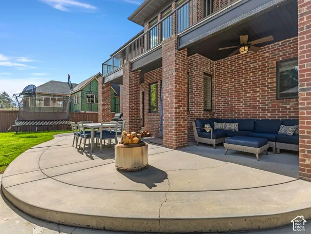 Covered brick patio featuring a curved concrete surface, metal railings on the upper balcony, and an outdoor ceiling fan