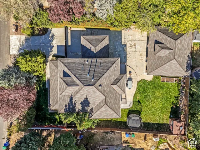 Aerial perspective of the property featuring a composition shingle roof, concrete driveway, detached garage, fenced yard, and mature landscaping